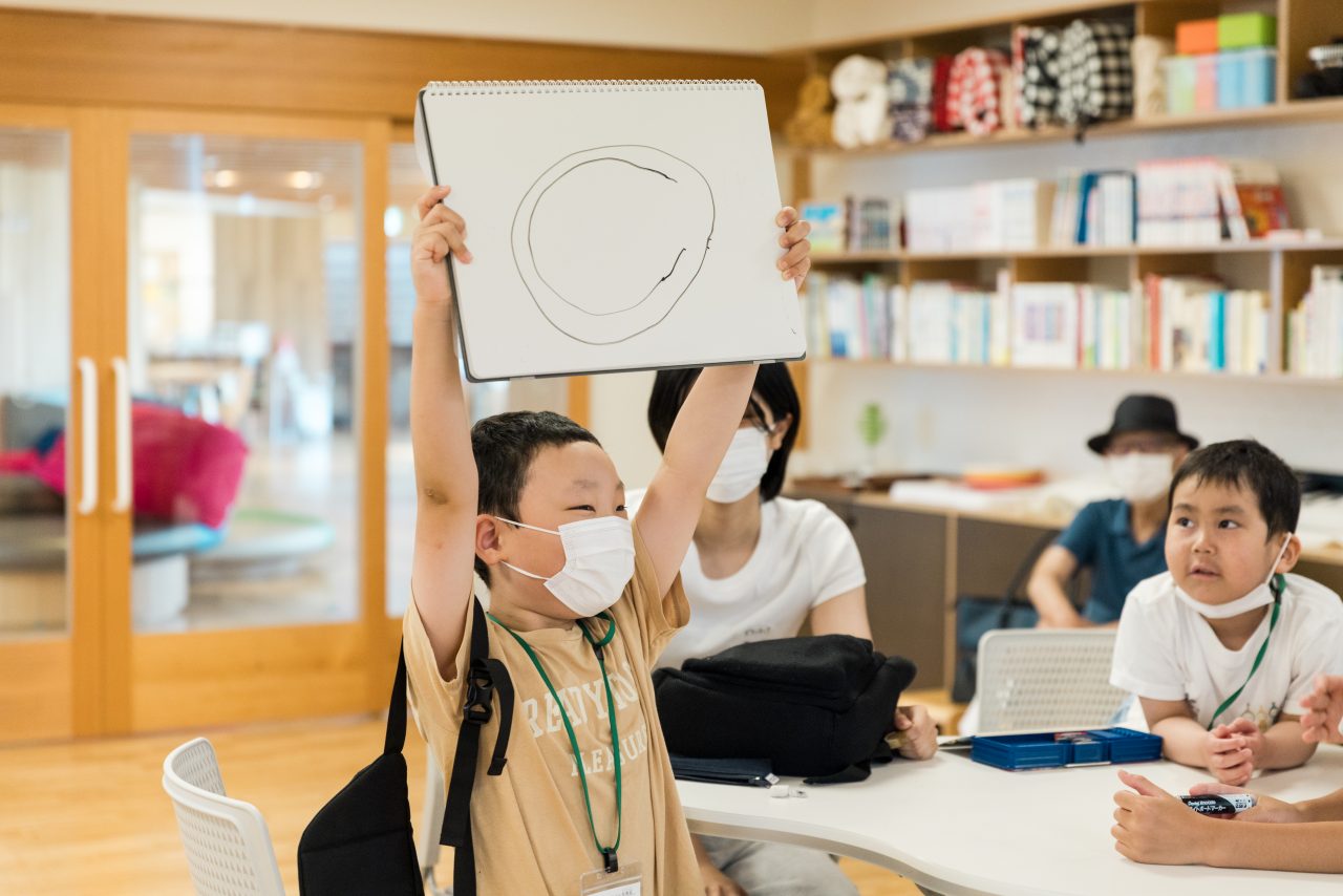 男の子がクイズの回答をかがげている様子